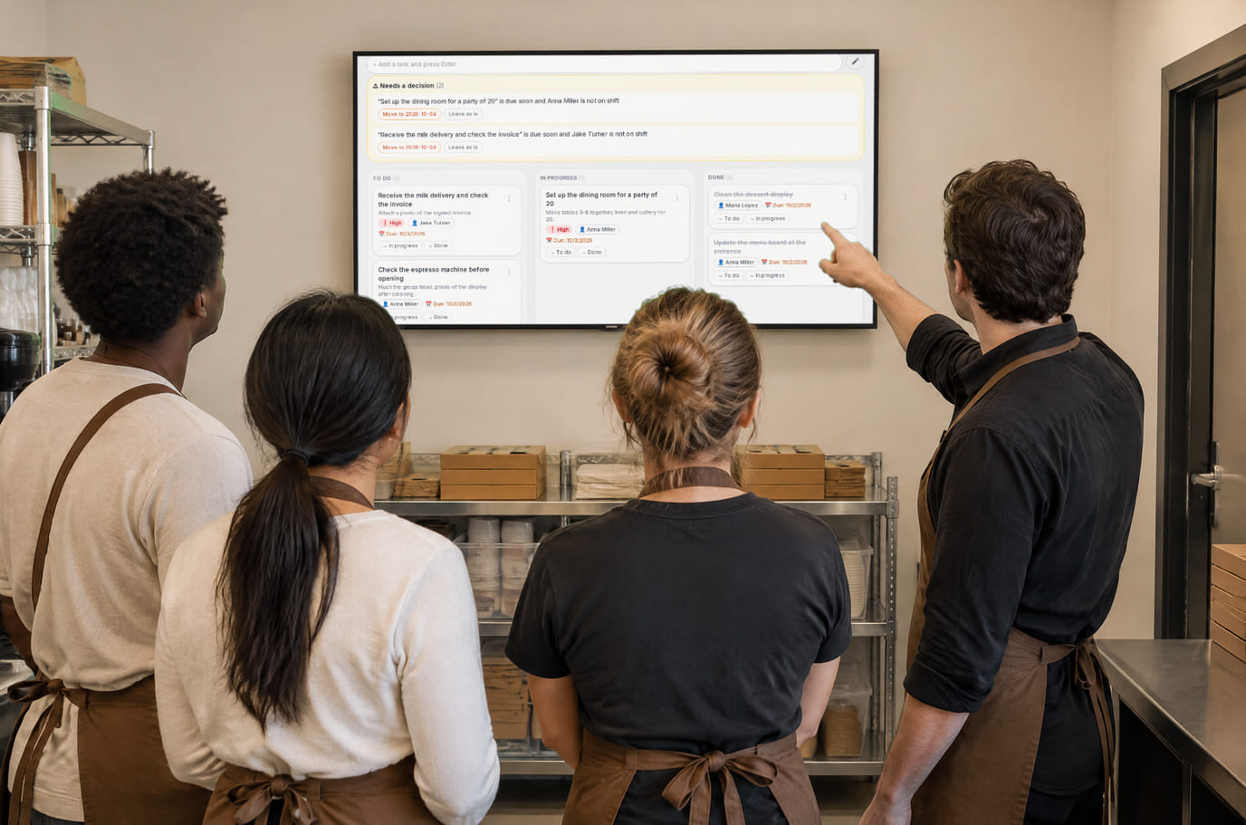 Morning briefing in a café back room: the manager shows the team the task board on a TV screen